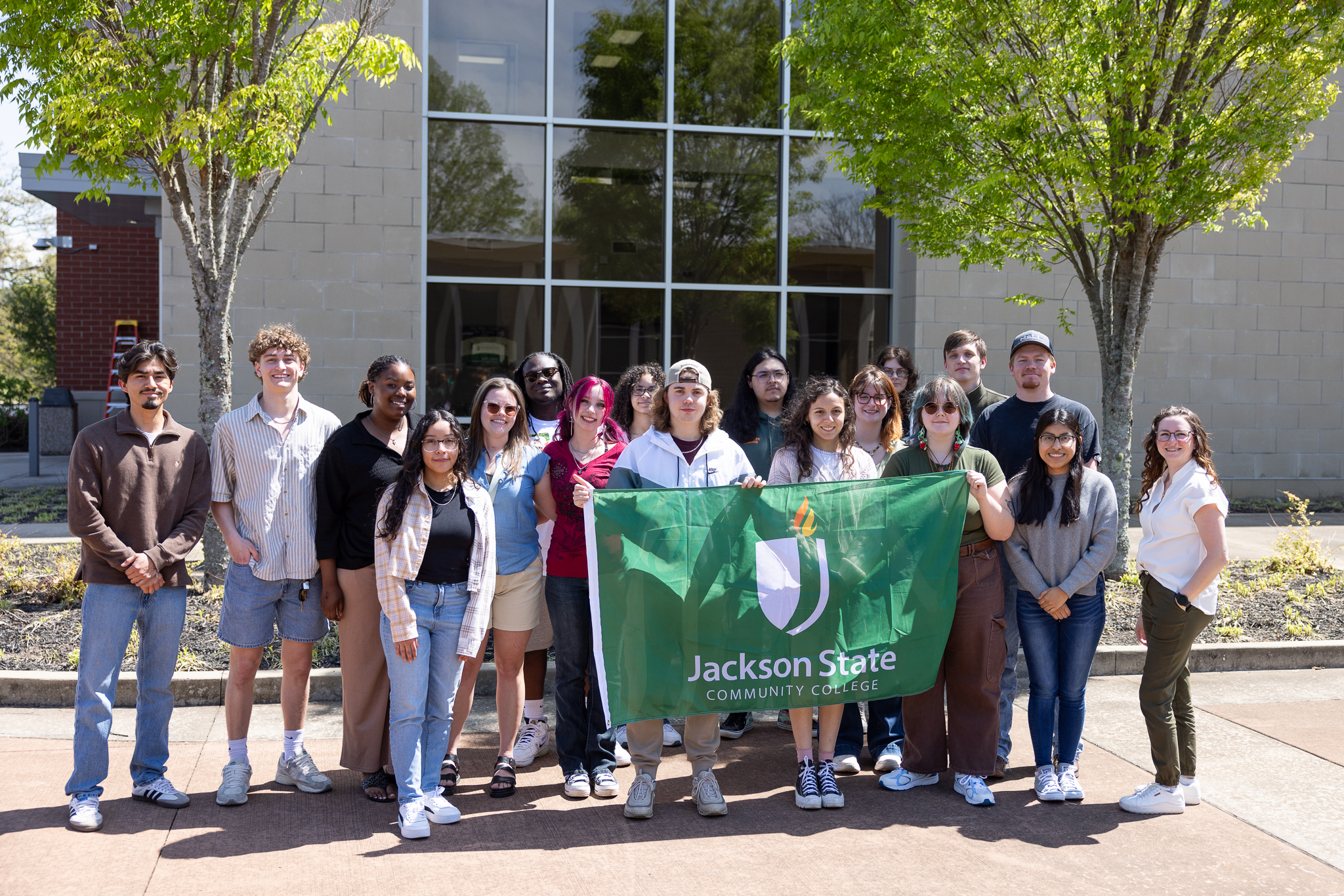 A group of Study Abroad students standing outside holding a green JSCC flag