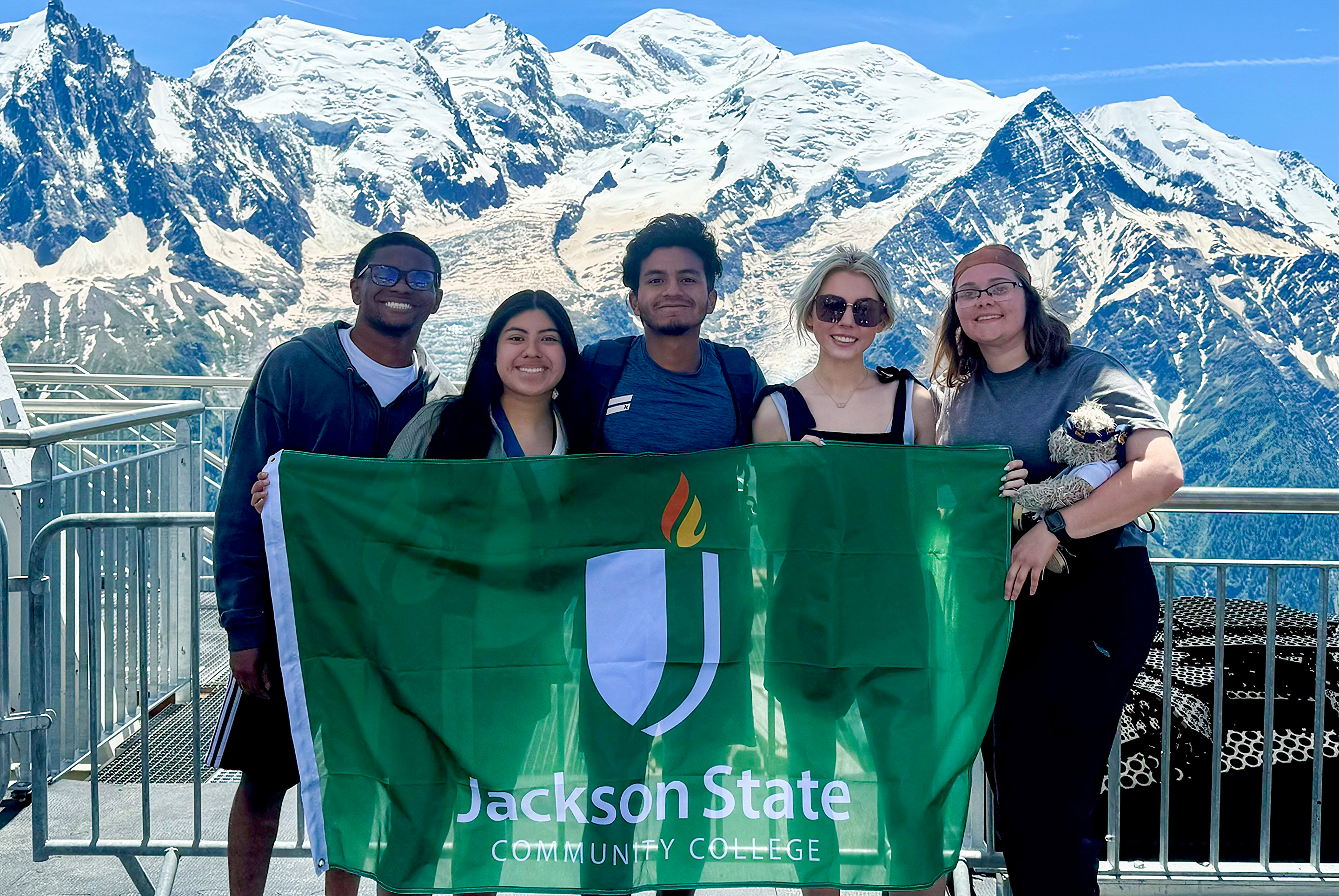Students with JSCC's Global Learning program pose in front of a snowy mountain range while holding a JSCC flag.