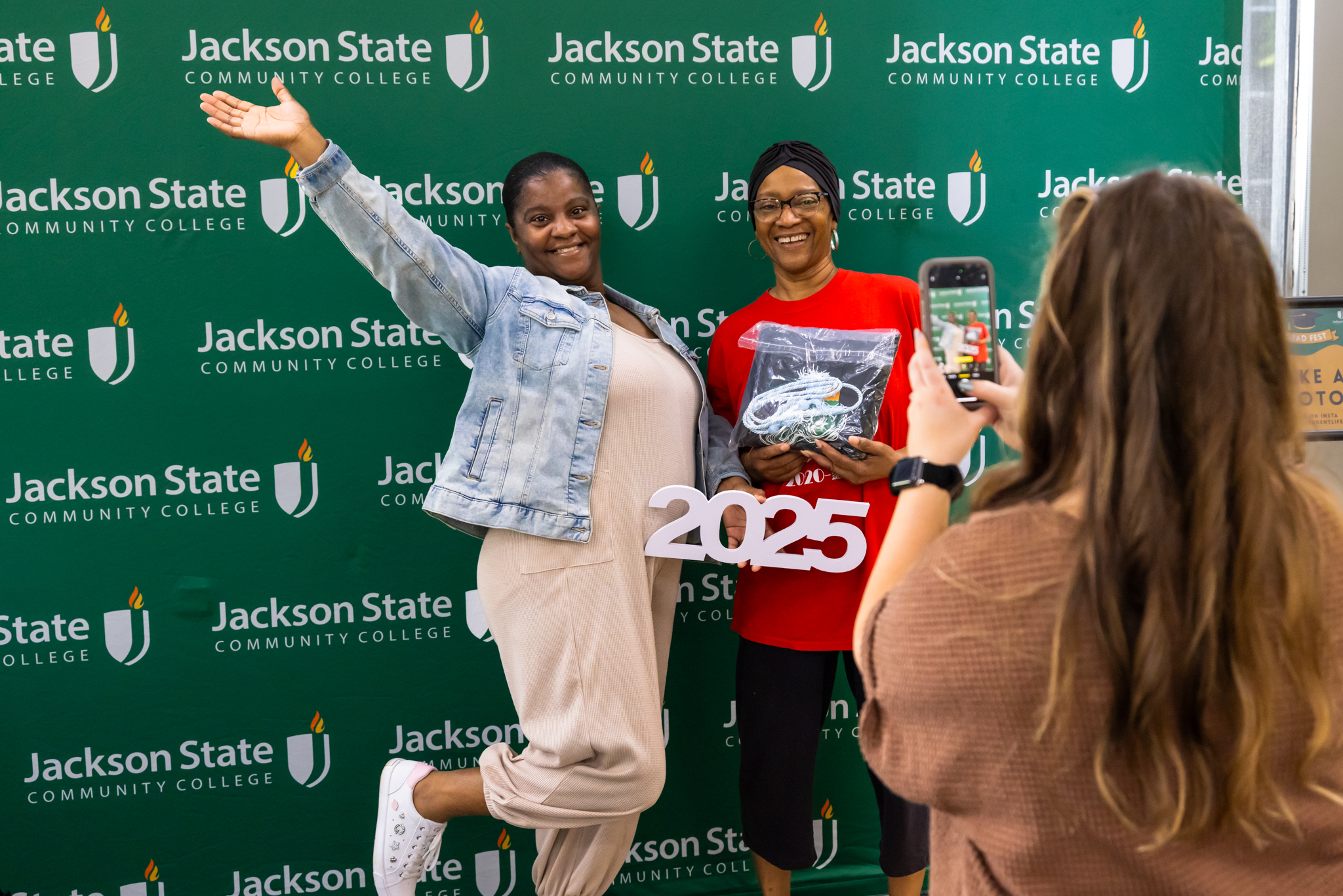 Two people pose for a photo in front of a JSCC backdrop.