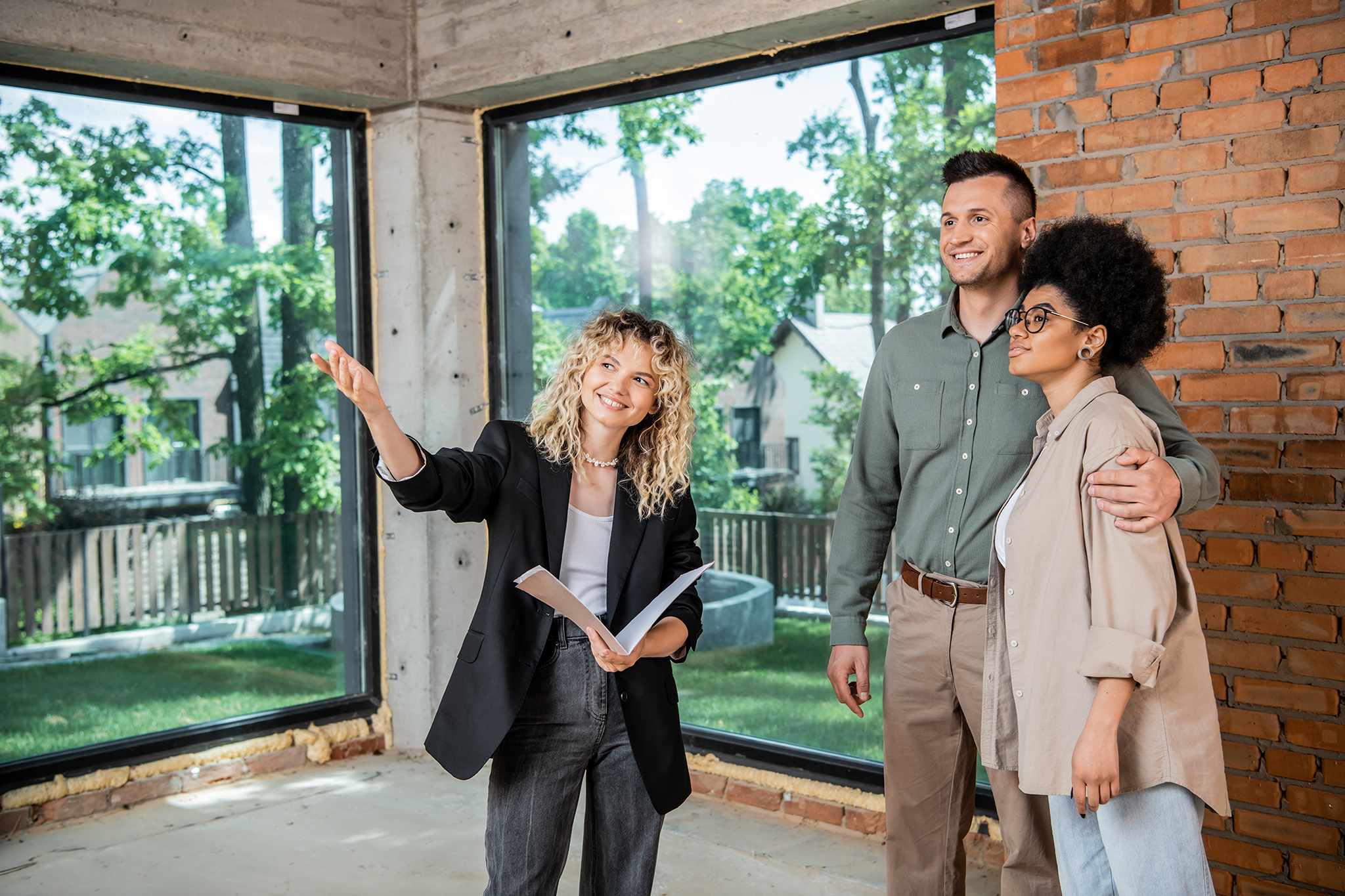 Image of a female real estate agent pointing to show the inside of a home to a couple that appear to be prospective buyers.