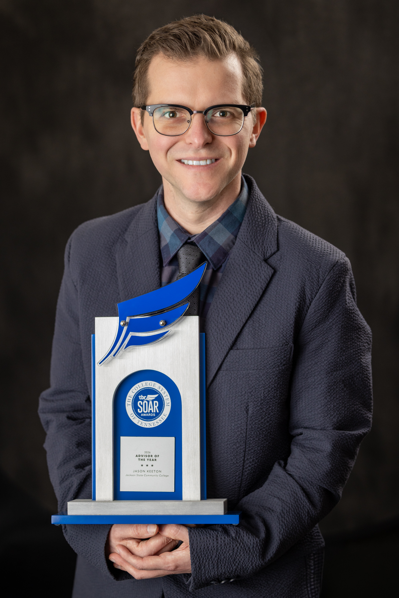 Studio portrait of Jason Keeton holding the SOAR Trophy for Advisor of the Year.